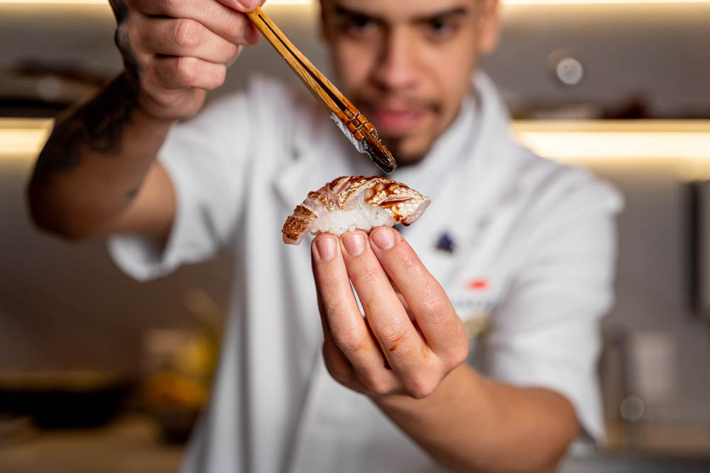 Chef segurando peça de nigiri em primeiro plano com iluminação cinematográfica